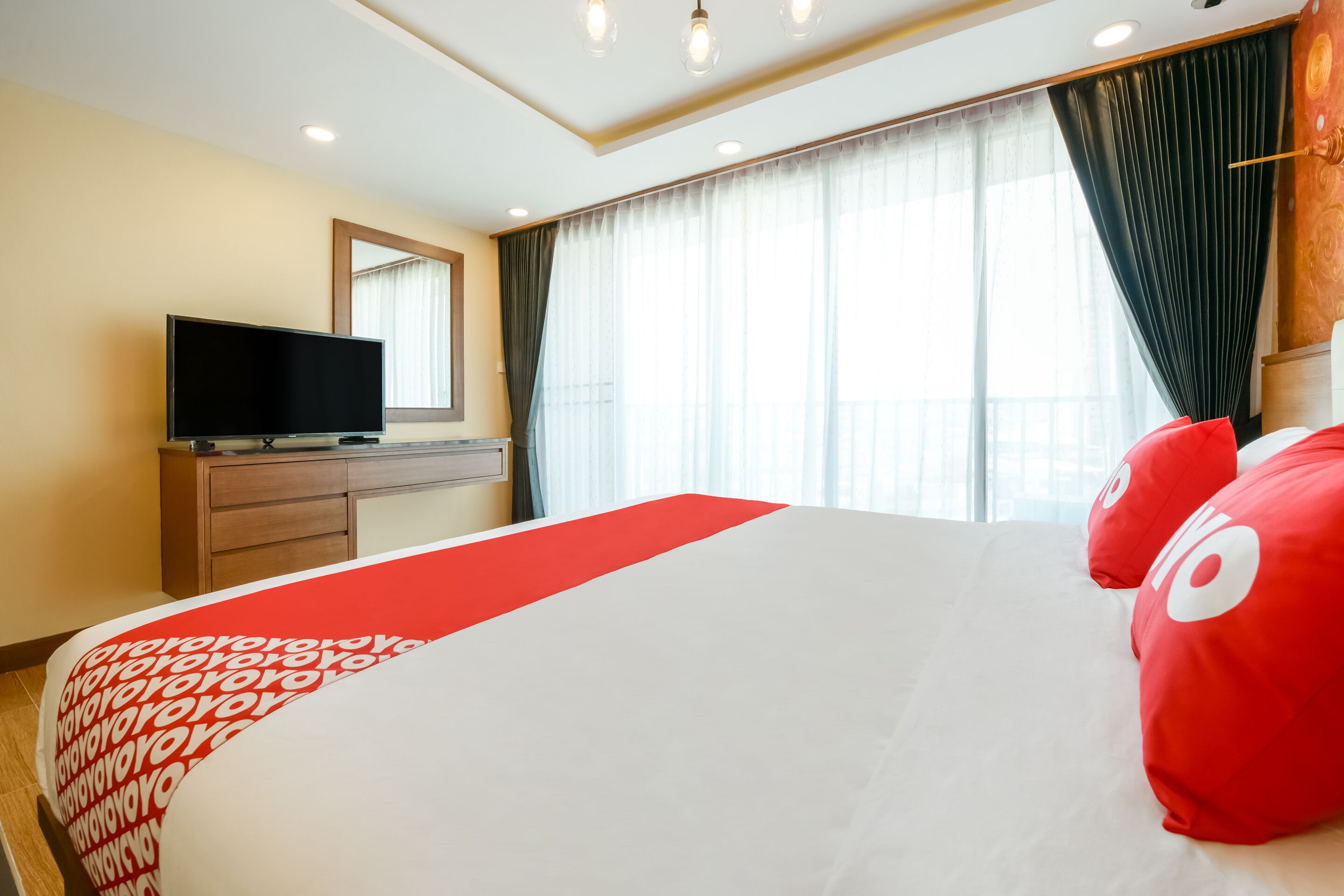 Una habitación de hotel con una cama grande, un televisor sobre un aparador de madera y una ventana con cortinas.