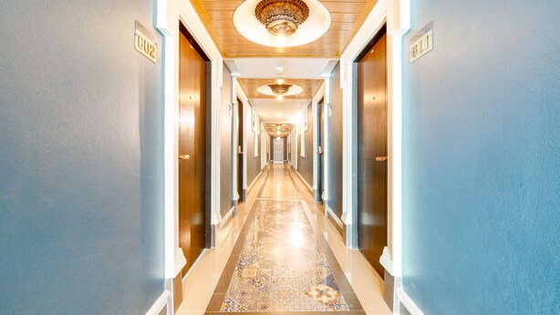 Un pasillo de hotel con piso pulido, techo decorativo y puertas con números de habitaciones.