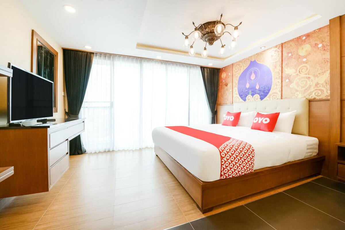 A hotel room with a large bed, a TV on a wooden desk, and a chandelier.