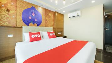 A hotel room with a large bed, a decorative wall mural, an air conditioning unit, and a wooden door.