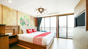 Habitación de hotel con una cama grande, un televisor montado en la pared, un balcón con vistas y un panel decorativo.