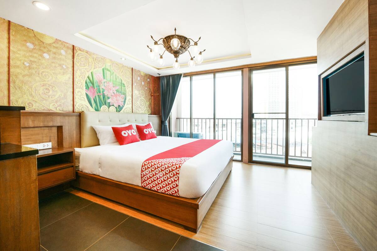 A hotel room with a large bed, a TV mounted on the wall, a balcony with a view, and a decorative wall panel.