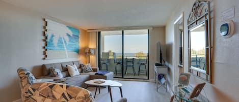 Una sala de estar con un sofá, sillones estampados, una mesa de centro de cristal y vistas al exterior a través de un ventanal corredero.