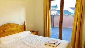 Une chambre à coucher avec un lit en bois, une petite table de chevet et une vue sur un balcon extérieur, accessible par une porte-fenêtre coulissante.