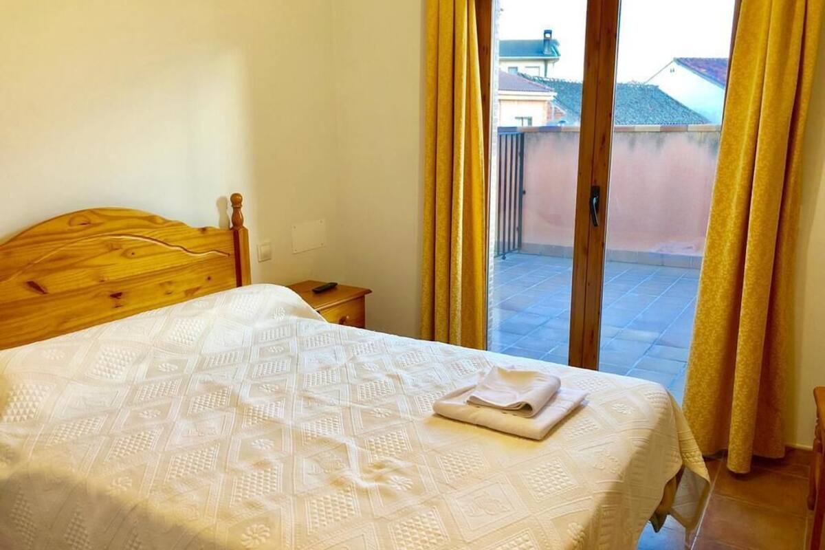 Un dormitori amb un llit de fusta, una petita taula de nit i vista a un balcó exterior a través d'una porta corredissa de vidre.