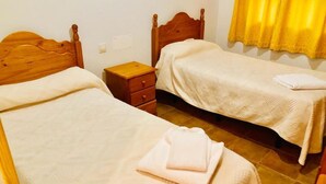 Une chambre avec deux lits en bois, une petite table de chevet en bois et un rideau jaune.