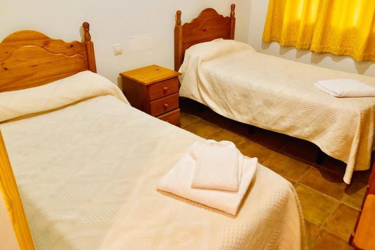 Habitació amb dos llits de fusta, una petita taula de nit de fusta i una cortina groga.