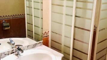 Un baño con lavamanos de mármol, dispensador de toallas y cabina de ducha con paredes de cristal.