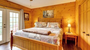 A wooden-paneled bedroom with a bed, a nightstand, a ceiling fan, and a door leading to a balcony.