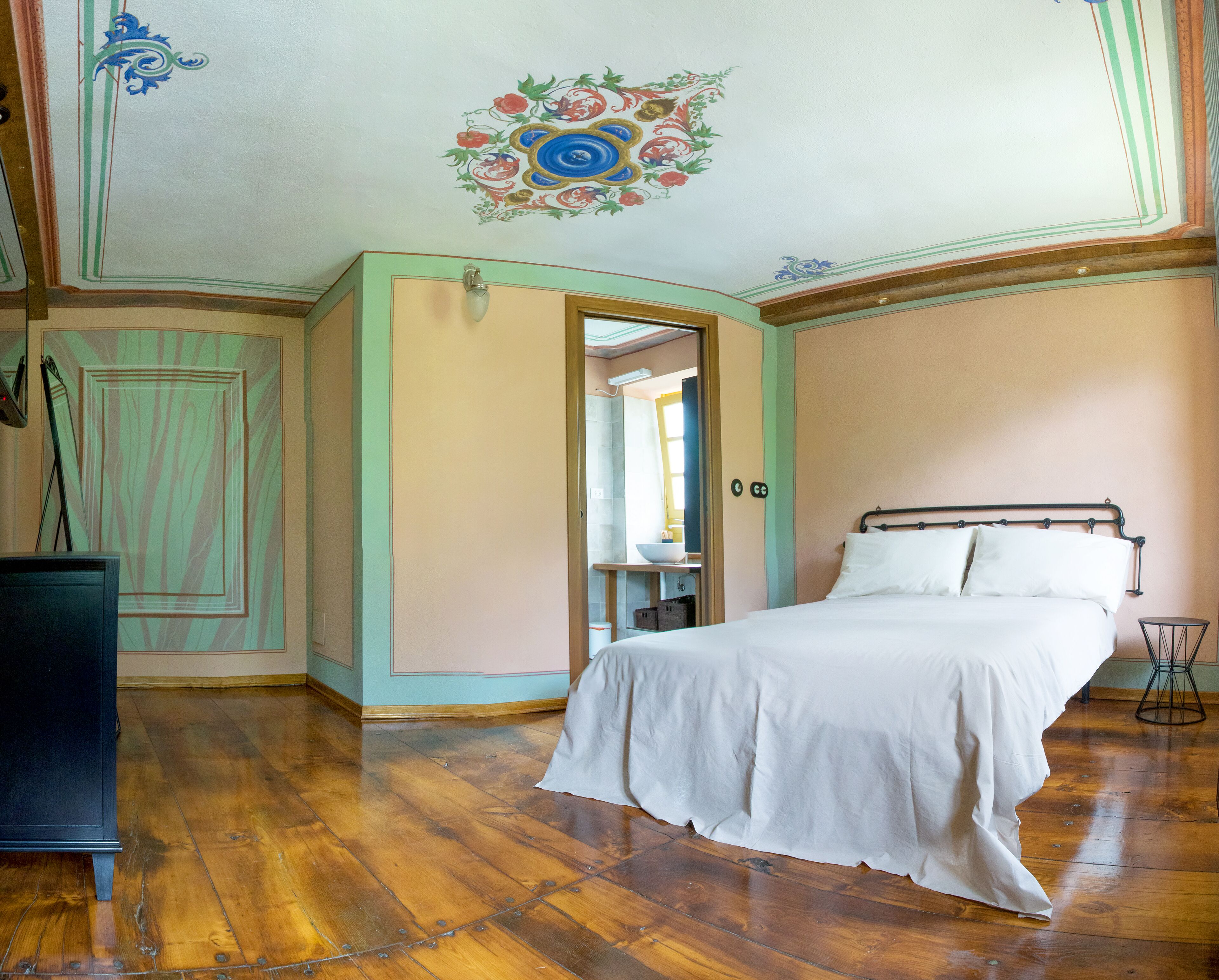 Una camera da letto con pavimento in legno, un letto con lenzuola bianche, un comò e uno specchio.