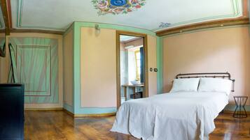 Una camera da letto con pavimento in legno, un letto con lenzuola bianche, un comò e uno specchio.