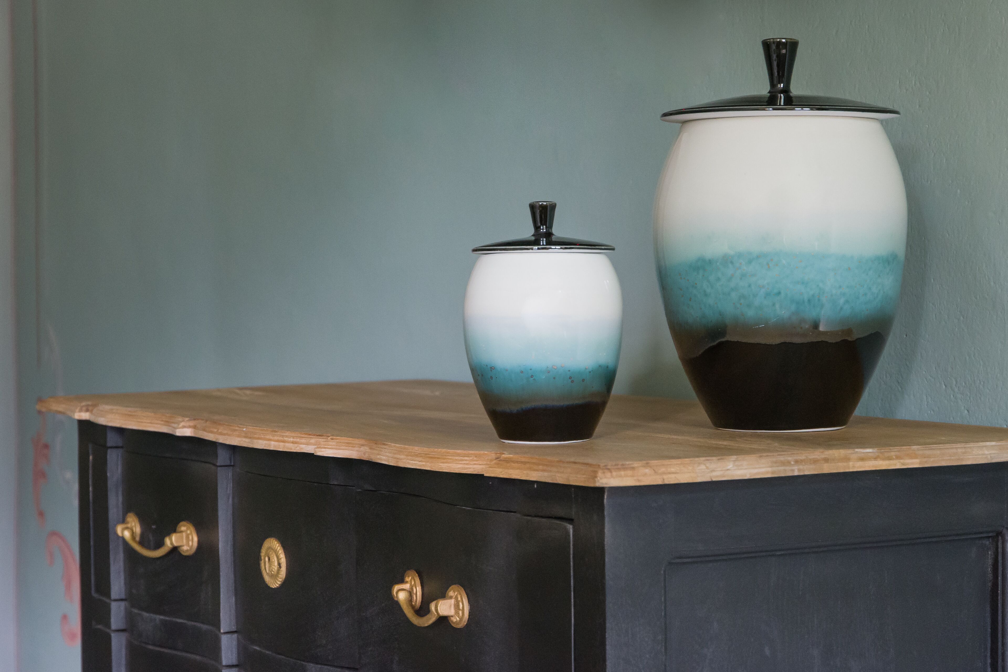 Due contenitori in ceramica su un piano di legno con un mobile nero sottostante.
