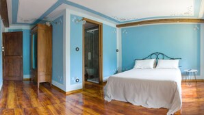 Een slaapkamer met een houten vloer, een bed met wit beddengoed, een houten kledingkast en een glazen deur naar een badkamer.