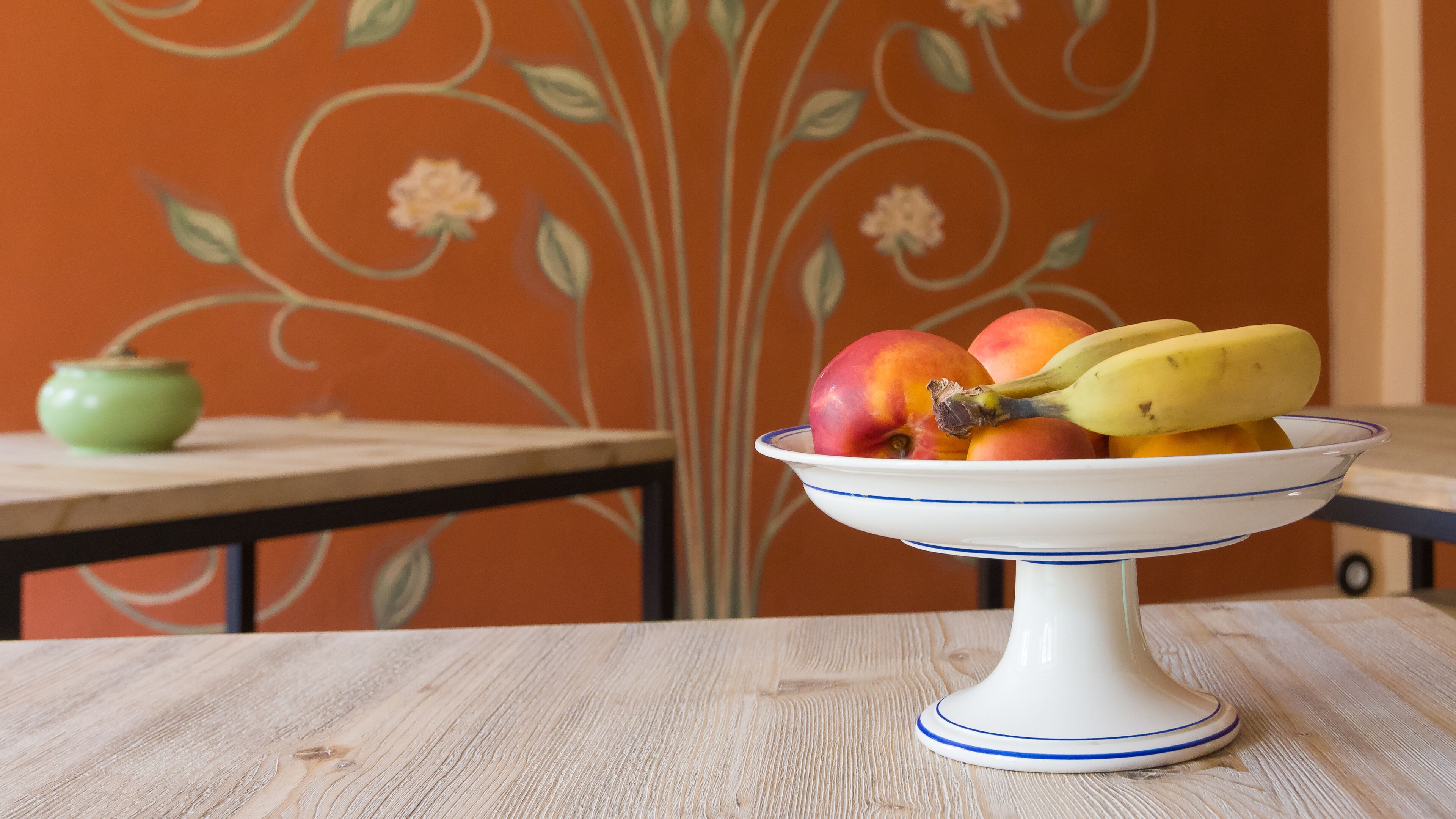 Un panier de fruits est posé sur une table, avec un papier peint à motifs floraux en arrière-plan.