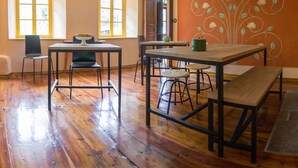 Een kamer met houten vloer, een eettafel met stoelen, een bankje en een decoratieve wand met bloemenmotieven.