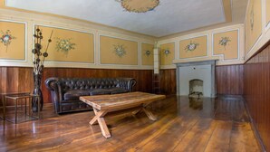 Een kamer met houten vloeren, een leren bank, een houten bijzettafeltje en een open haard.