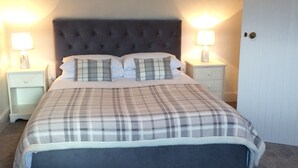 A bedroom with a tufted headboard, a plaid bedspread, two bedside tables with lamps, and a door to the right.