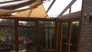 A conservatory with a table and chairs, large windows, and a stone wall.