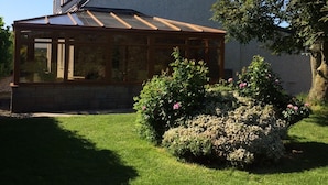A house with a conservatory, a garden with flowers, and a clear blue sky.