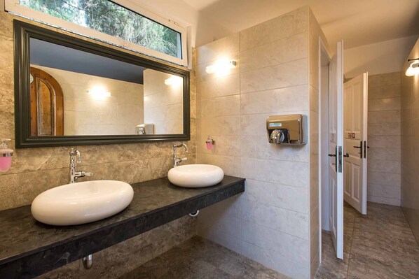 A modern bathroom with two sinks, a large mirror, and a built-in soap dispenser.