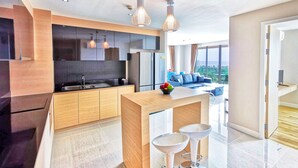 A modern kitchen with a central island, a dining area with bar stools, a large TV, and a view of the outdoors. - Grande Caribbean Resort (Pattaya)