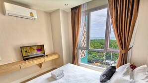 A hotel room with a bed, a desk with a laptop, a window with curtains, and an air conditioning unit. - Grande Caribbean Resort (Pattaya)