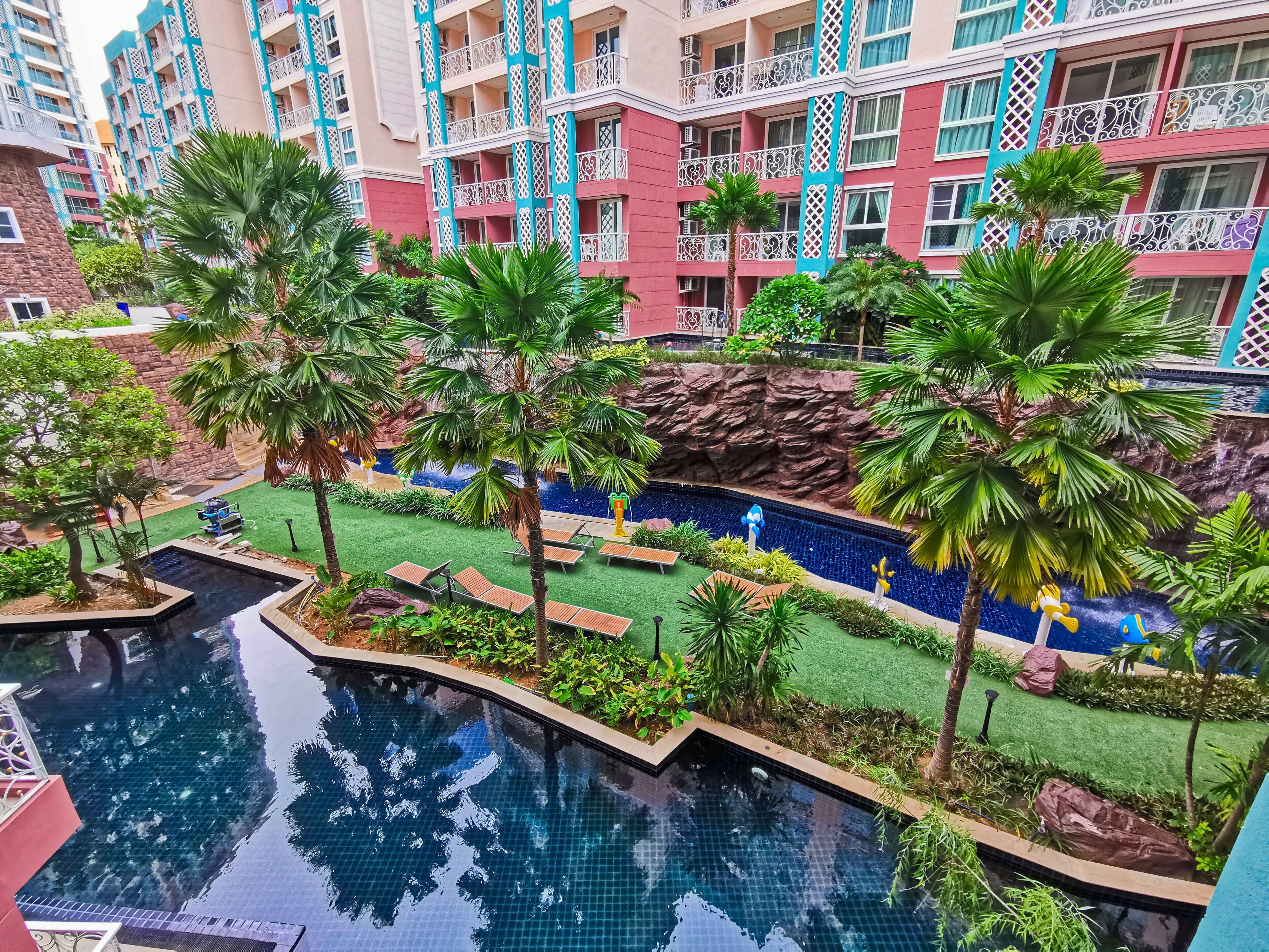 A swimming pool with a rock wall and palm trees, surrounded by a well-maintained lawn and lounge chairs.