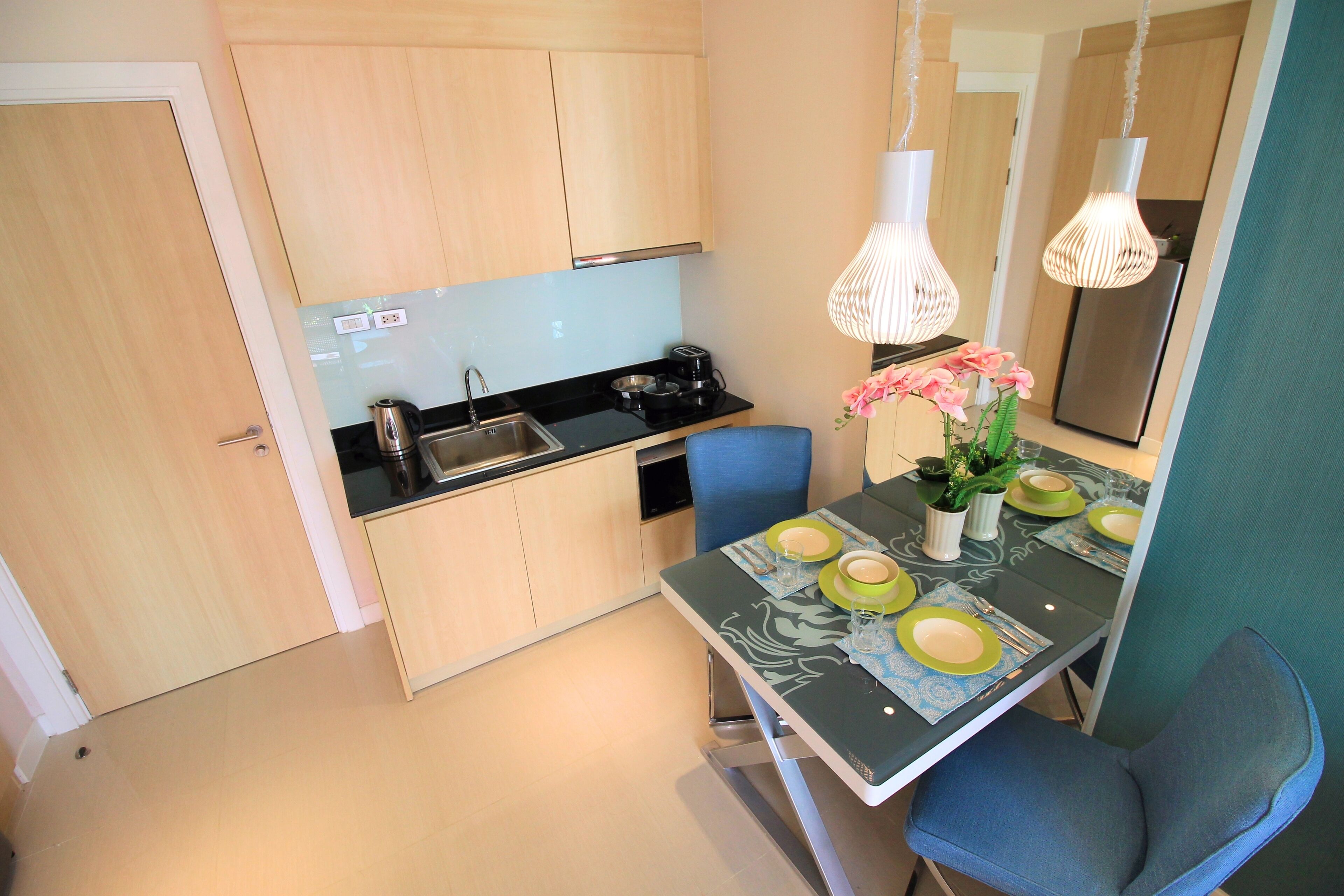 A modern kitchen with wooden cabinets, a black countertop, and a dining table set with green plates and pink flowers.