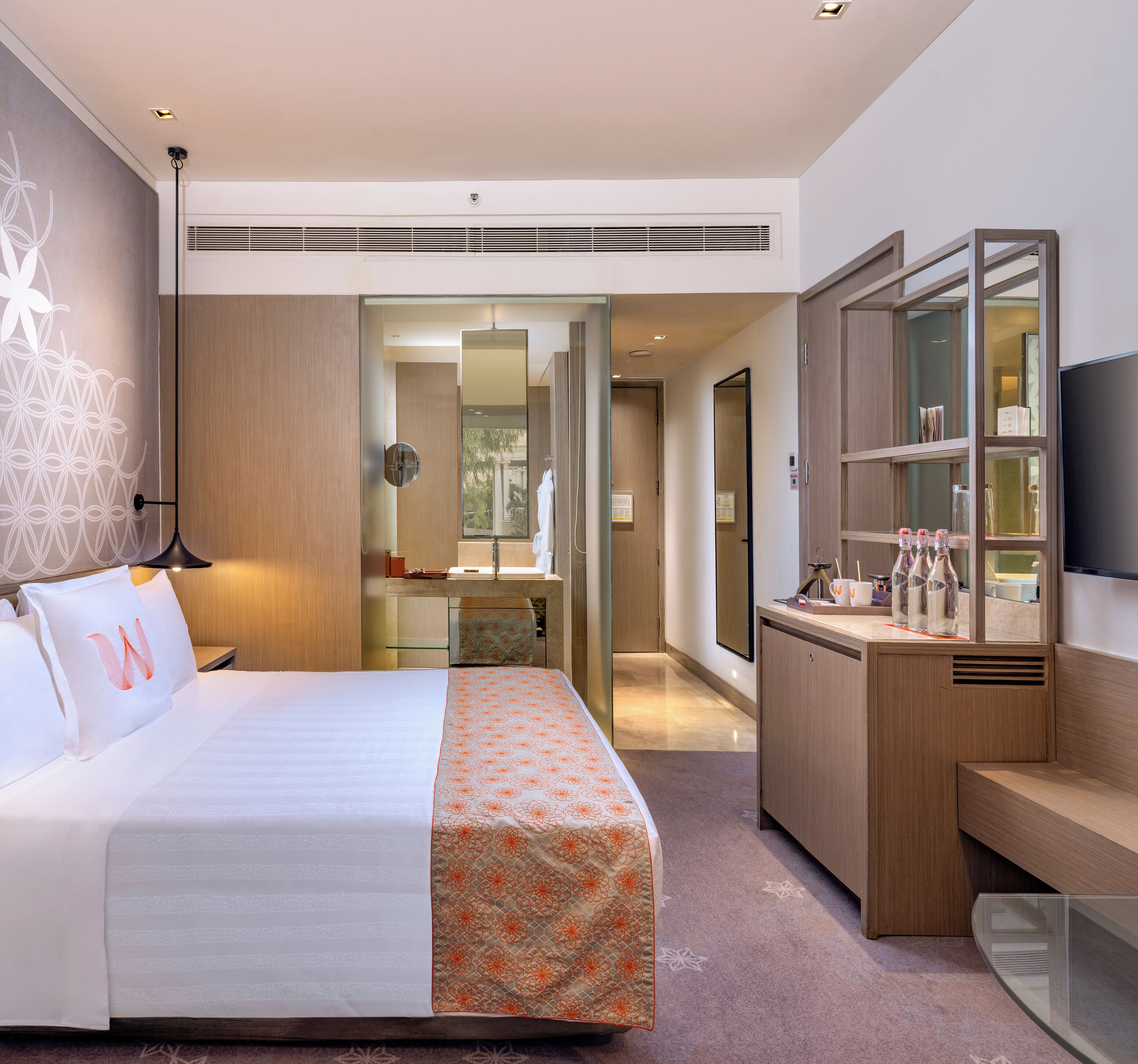 A modern hotel room with a large bed, a desk, a mirror, and a TV.
