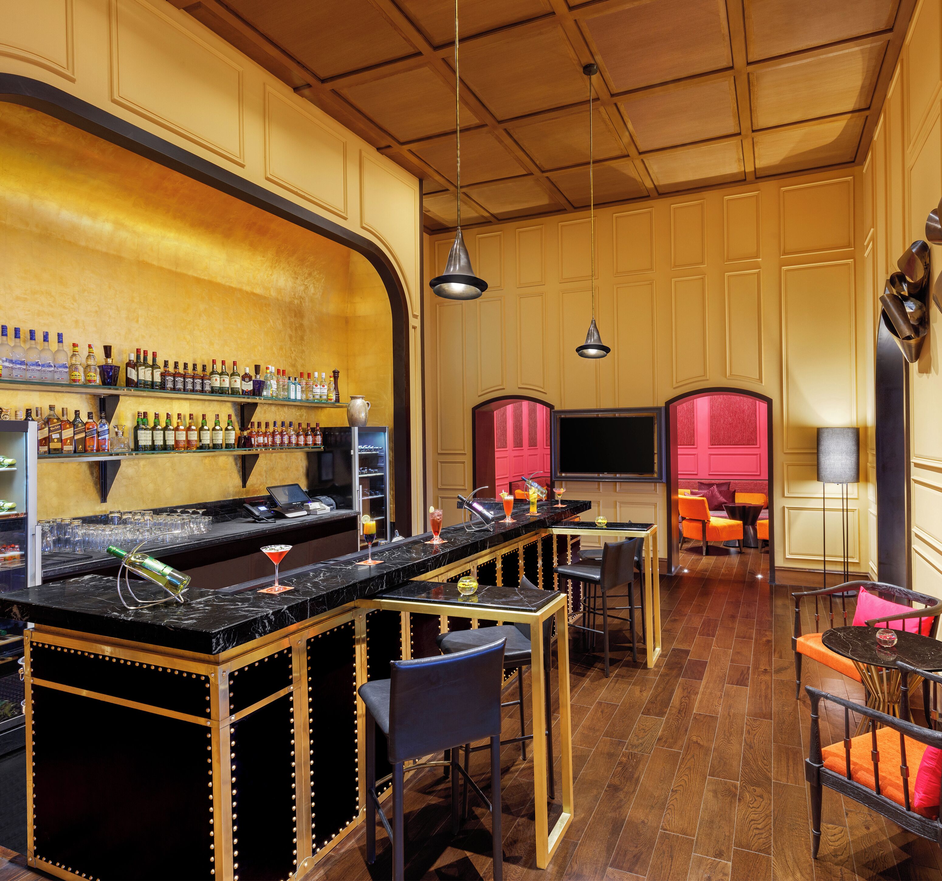 A bar area with a long counter, multiple shelves of bottles, and bar stools.