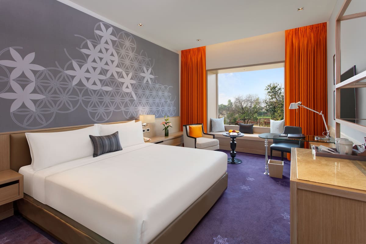A modern hotel room with a large bed, a desk, a chair, and a view of the outdoors.