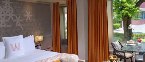 A hotel room with a bed, a sofa, a dining table with a glass top, and a view of the outdoors.