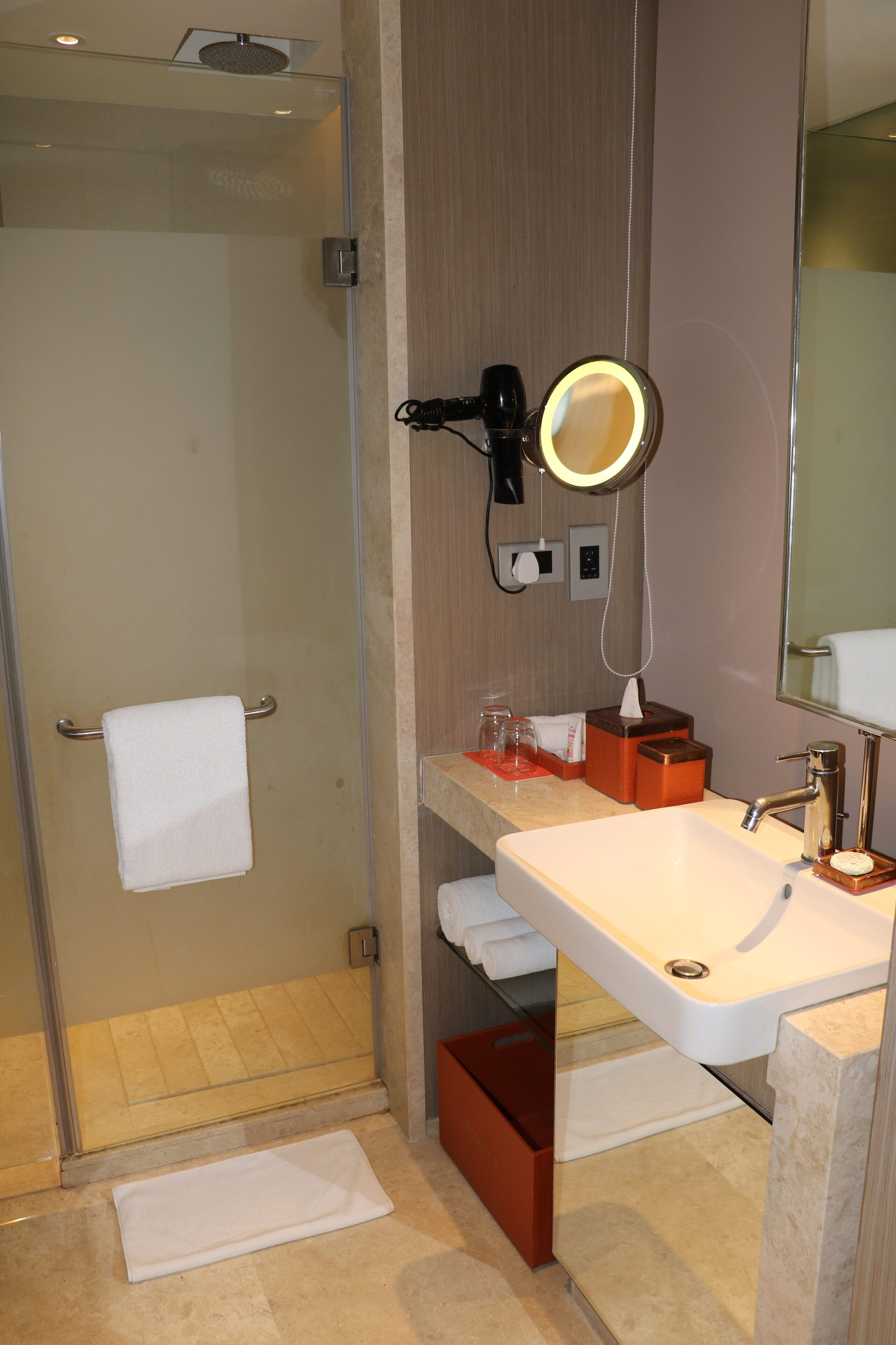 Un baño con cabina de ducha de vidrio, un lavamanos blanco con espejo y un perchero para toallas.