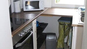 A compact kitchenette with a microwave, oven, and a small window with blinds.
