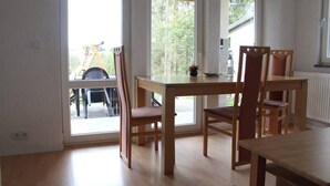 A dining area with a wooden table and chairs, large windows, and a view of outdoor furniture.