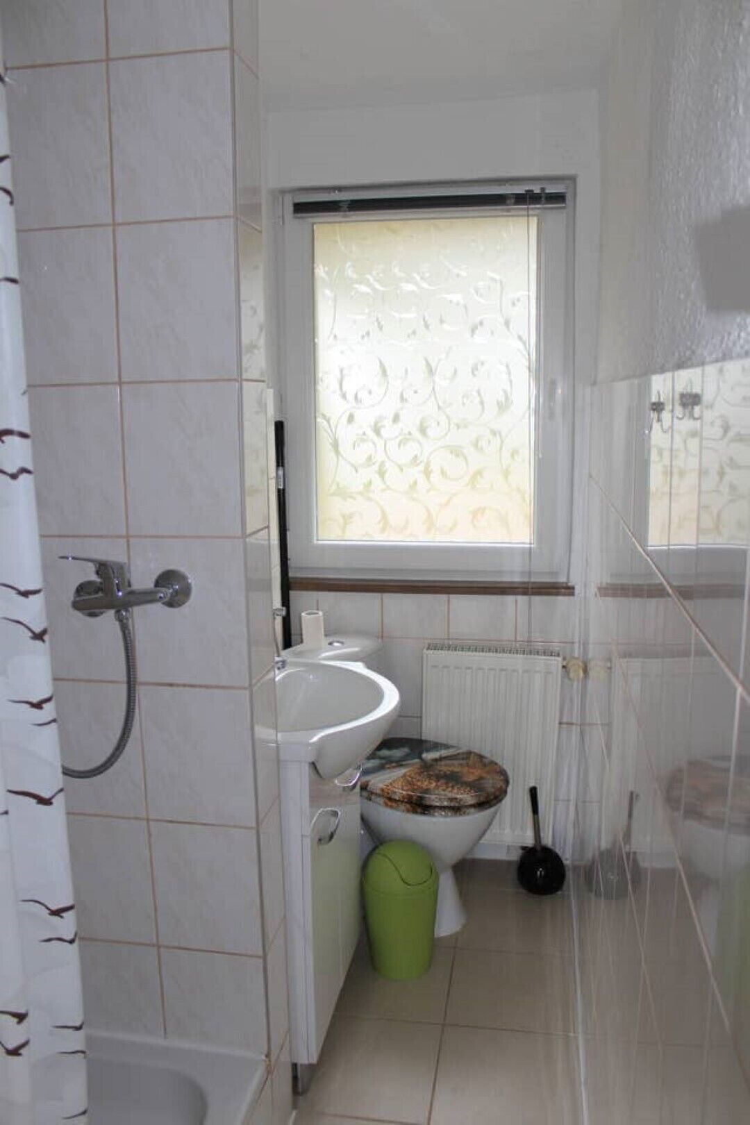 A bathroom with a toilet, sink, shower, and a window with a decorative pattern.