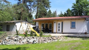 A house with a red roof, a wooden deck, and a small garden area with rocks and grass.