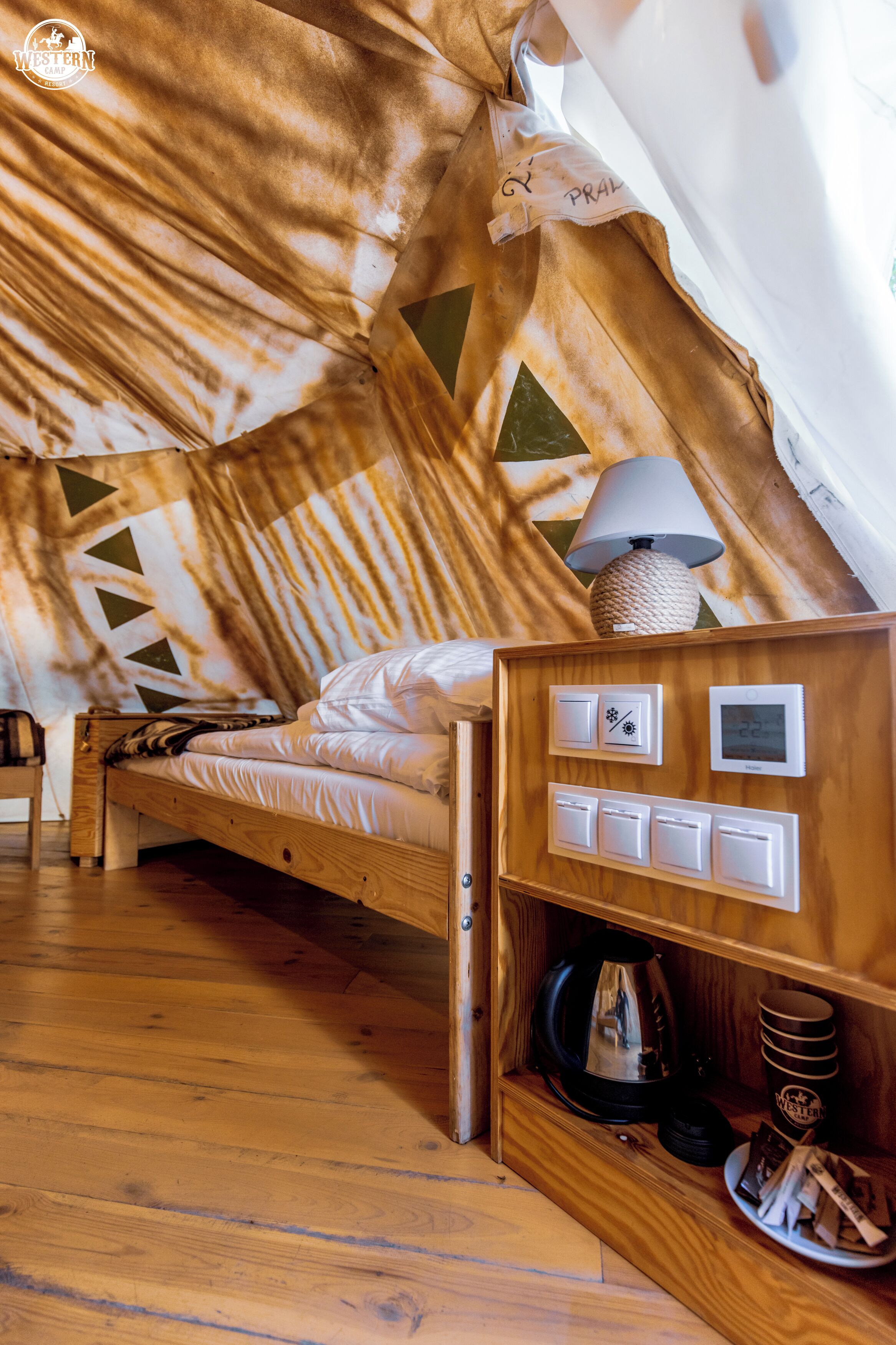 A cozy attic bedroom with a wooden bed, a lamp, a thermostat, and a coffee maker.