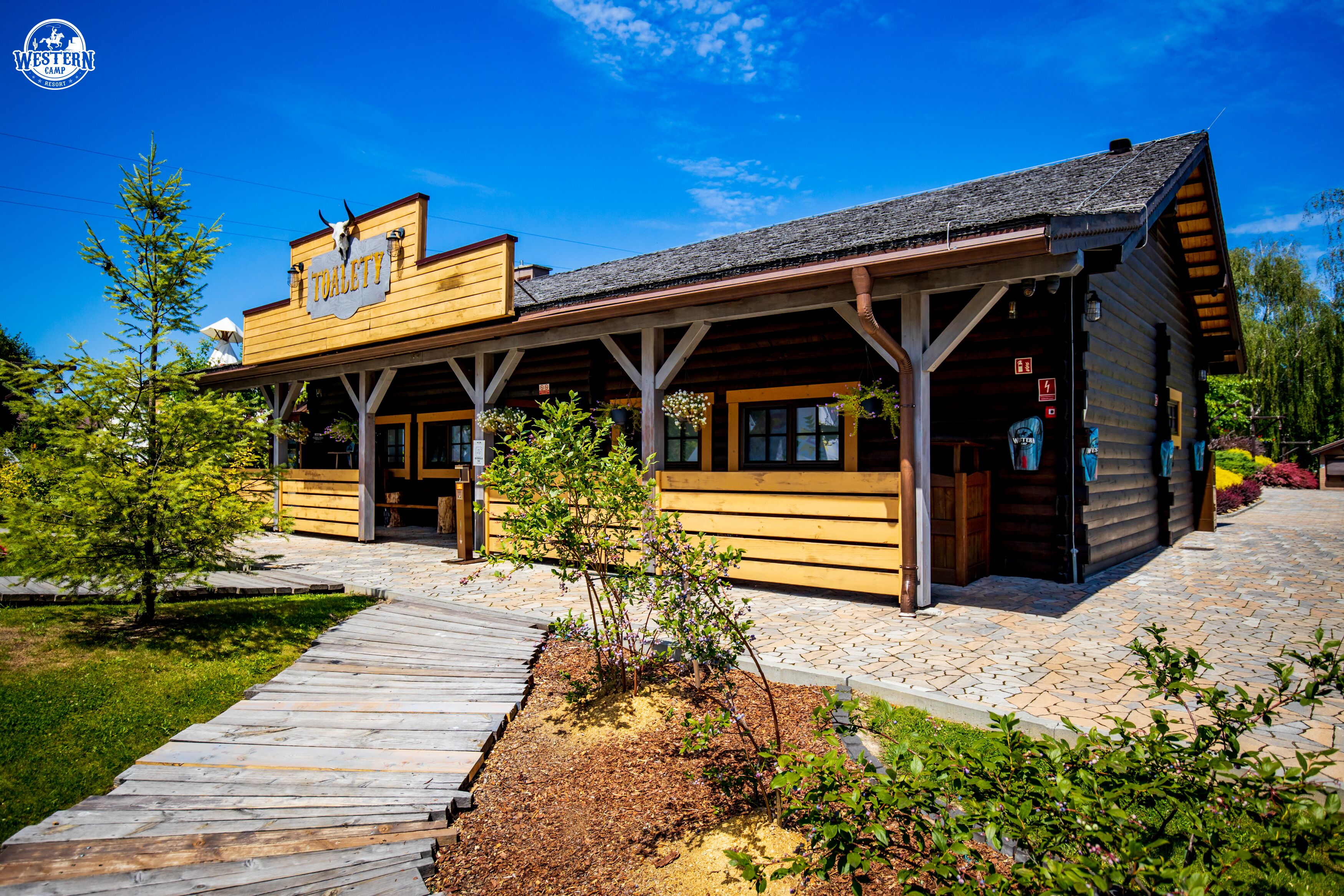 A Western-themed building with a wooden facade, a covered porch, and a sign reading "TOILET".