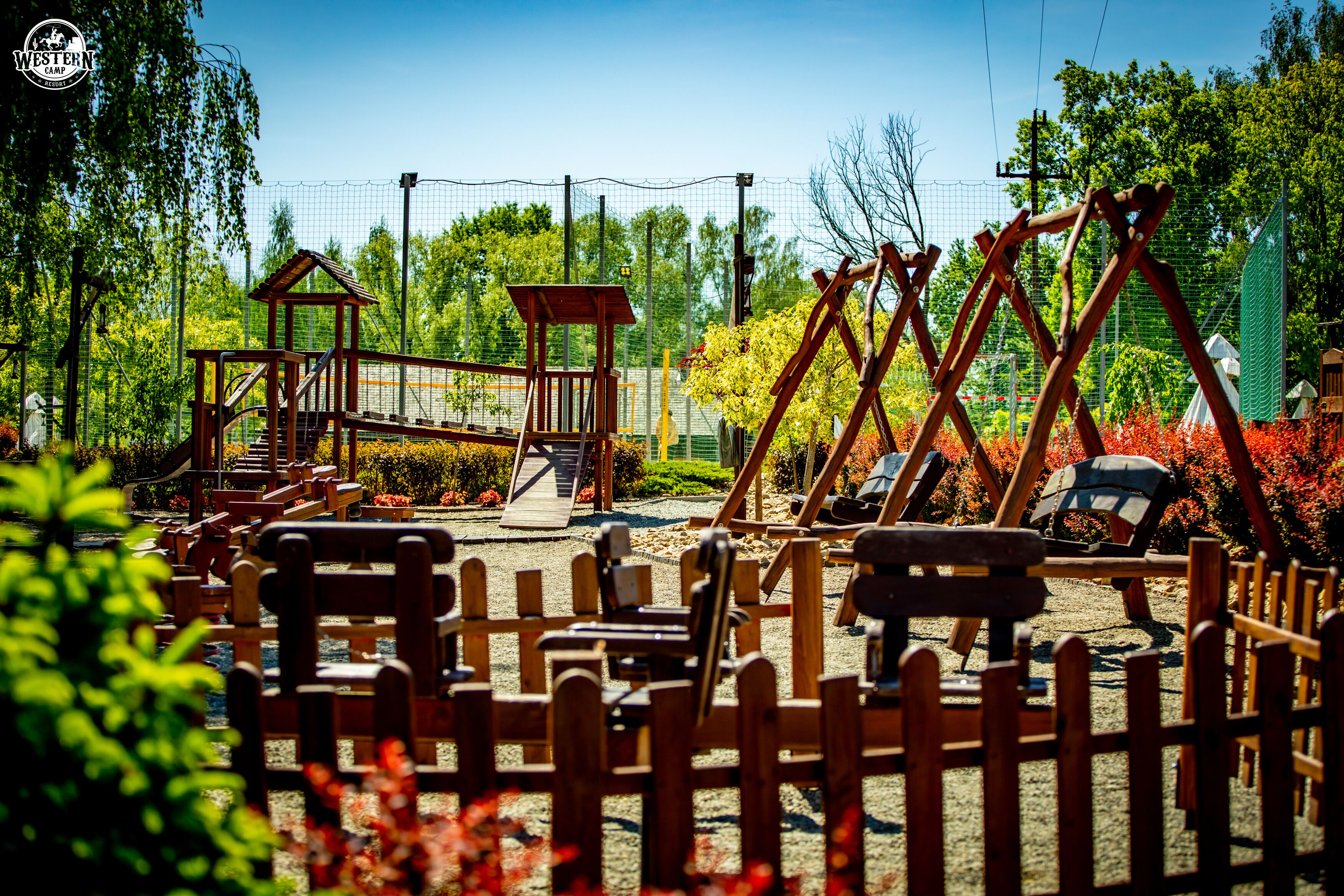 A playground with wooden structures, a small house, and a fenced area with benches.