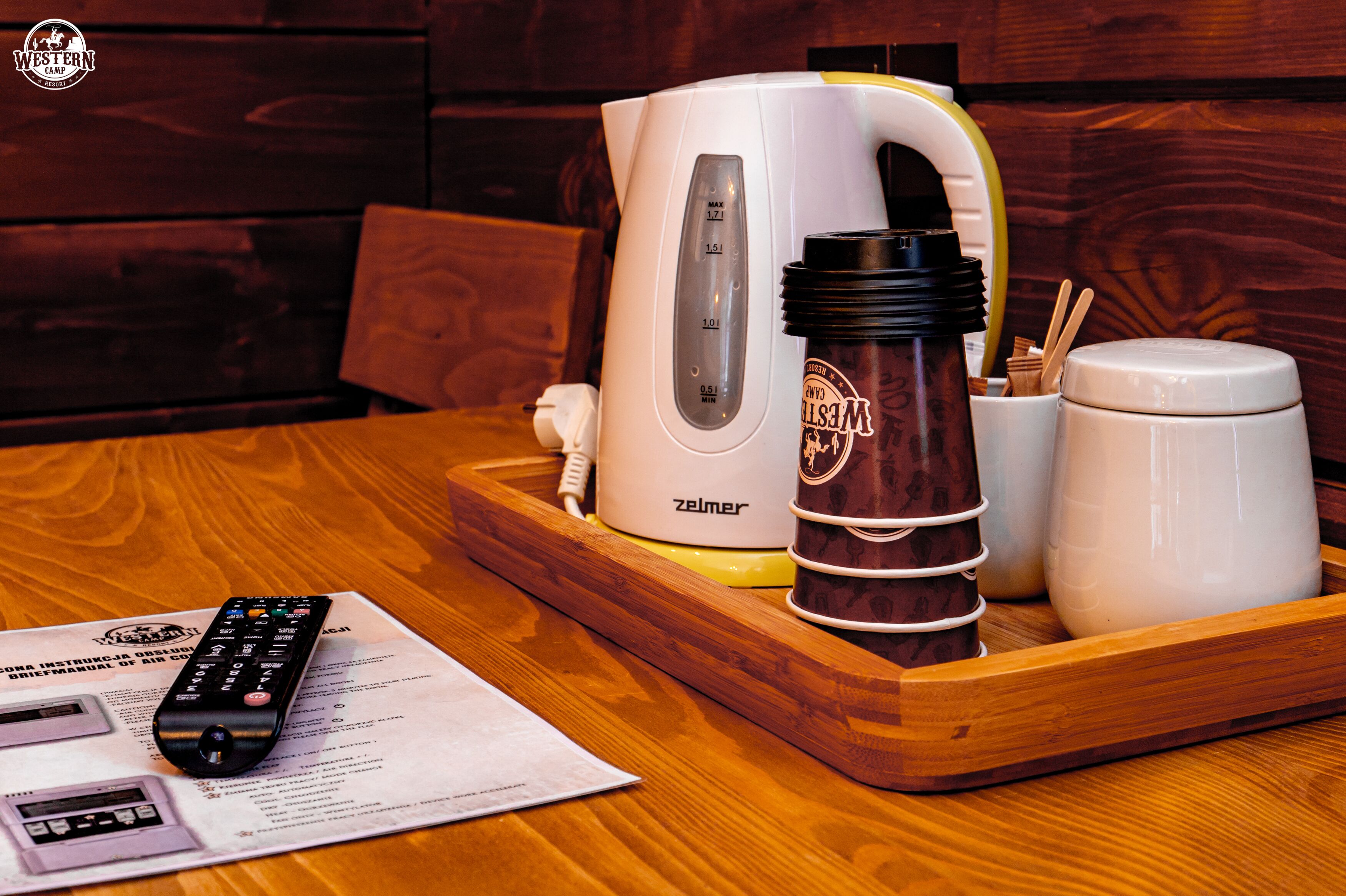 A wooden table with a white kettle, a brown mug, a white cup, and a remote control.