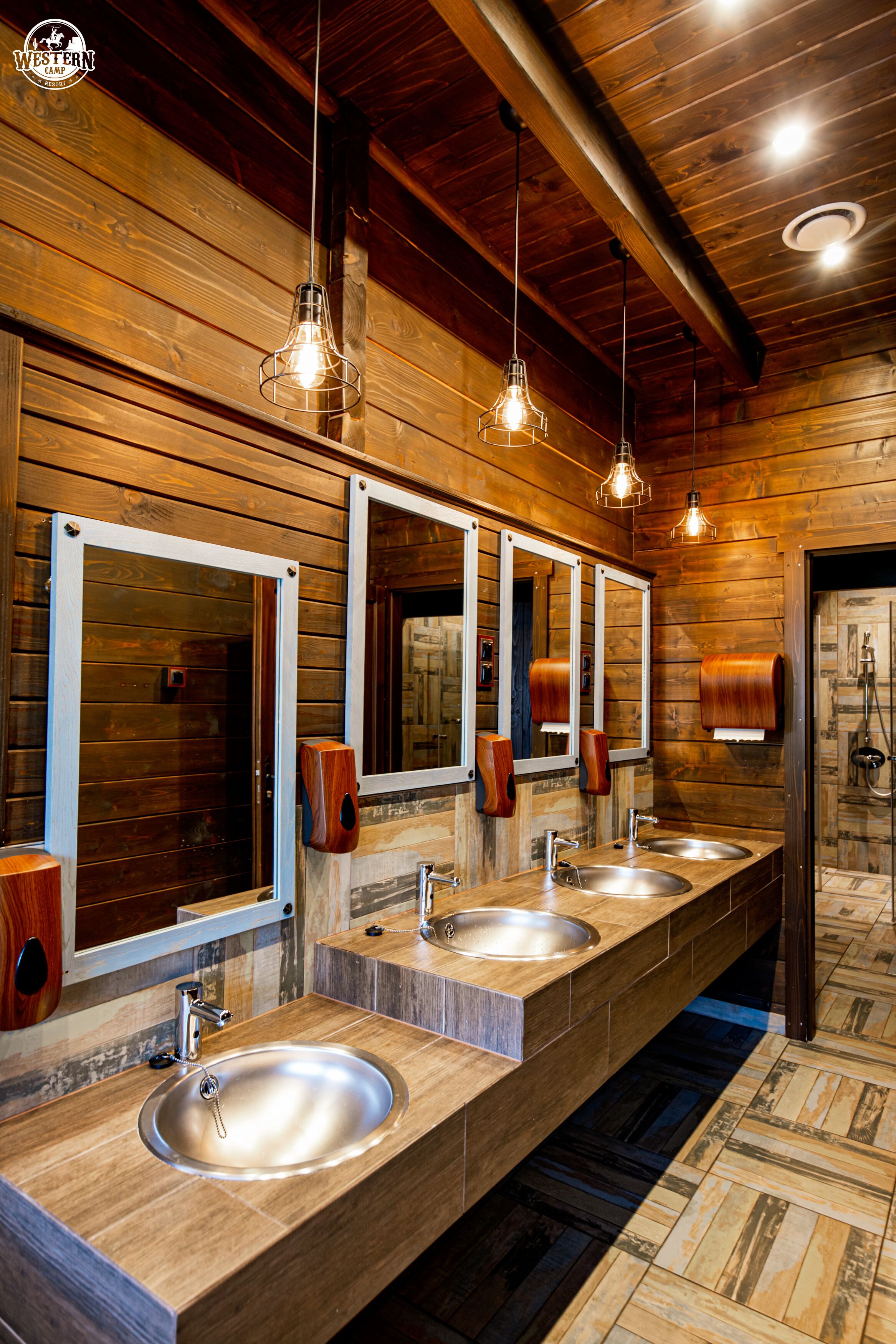 Une longue salle de bain en bois, dotée de trois lavabos, de miroirs et de luminaires suspendus.