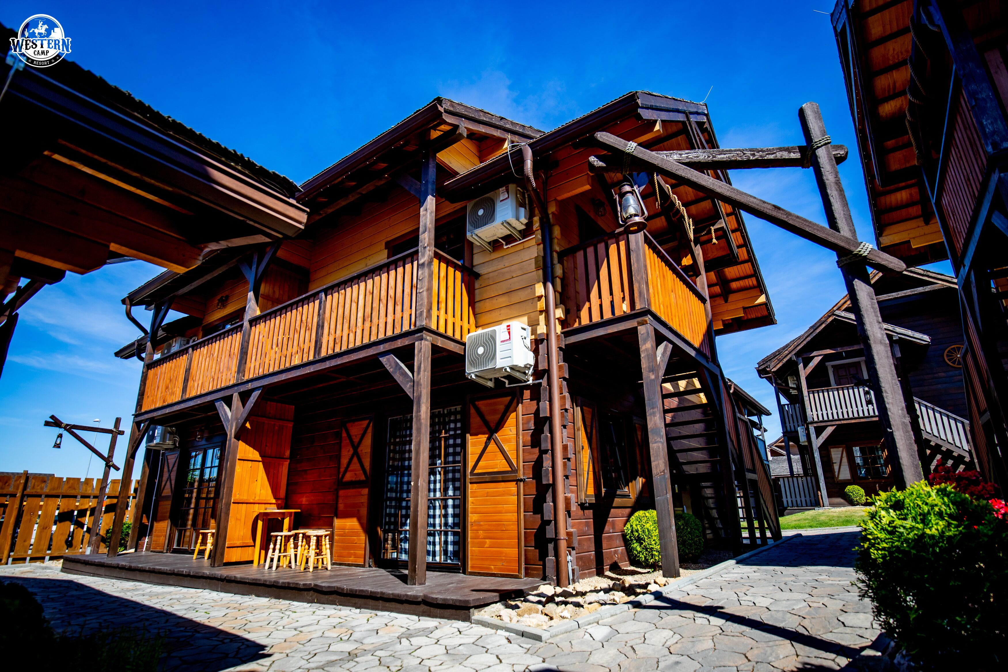 A wooden cabin with a balcony, a stone-paved entrance, and a clear blue sky.