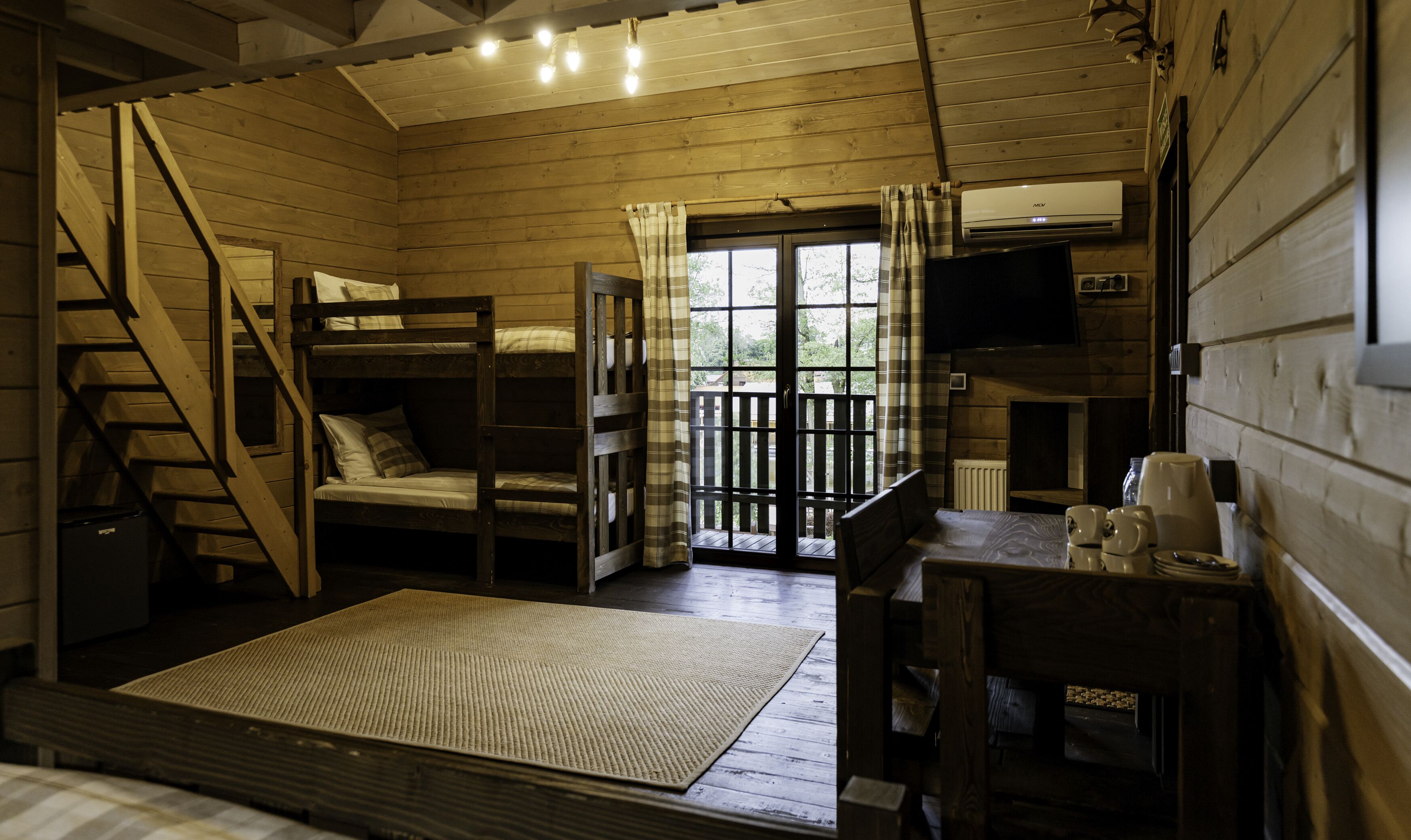 A cozy cabin with a bunk bed, a small table with cups, a TV, and a staircase.