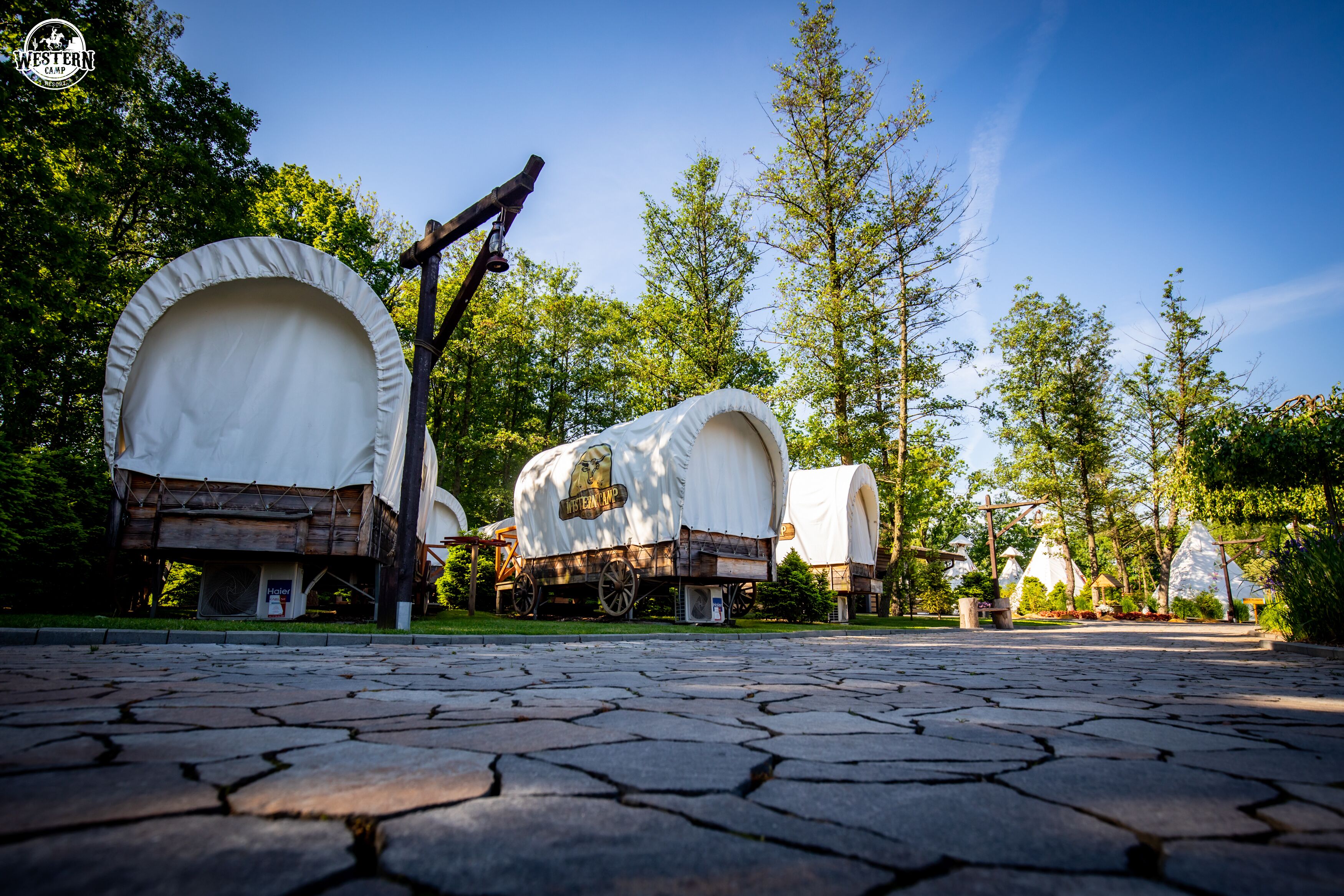 A rustic campsite with covered wagons and wooden structures.