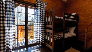 Una habitación tipo cabaña con una cama litera de madera, cortinas a cuadros y vistas a través de un ventanal.