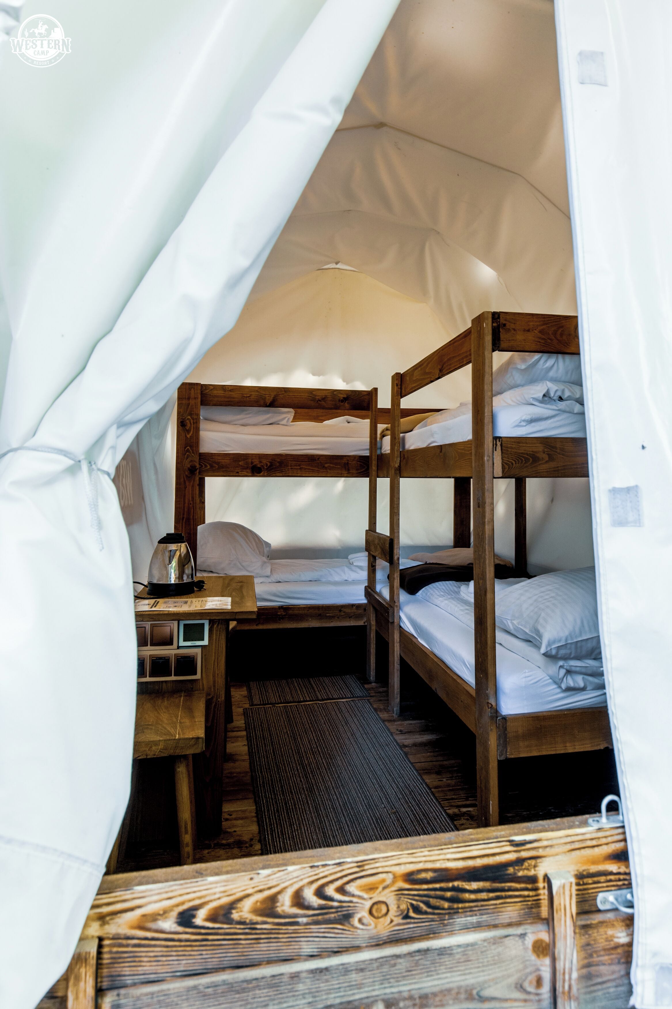 A bunk bed room with a wooden desk and a small table, a curtain, and a bench.
