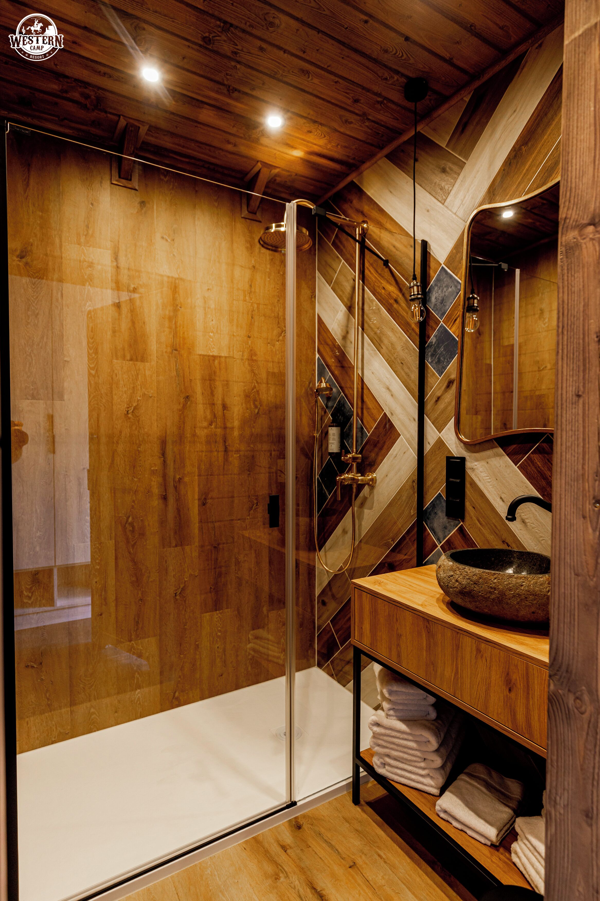 Un baño moderno con paneles de madera, cabina de ducha de vidrio, tocador de madera con lavamanos de piedra y un espejo sobre el lavamanos.