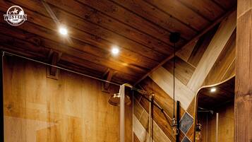 Un baño moderno con paneles de madera, cabina de ducha de vidrio, tocador de madera con lavamanos de piedra y un espejo sobre el lavamanos.
