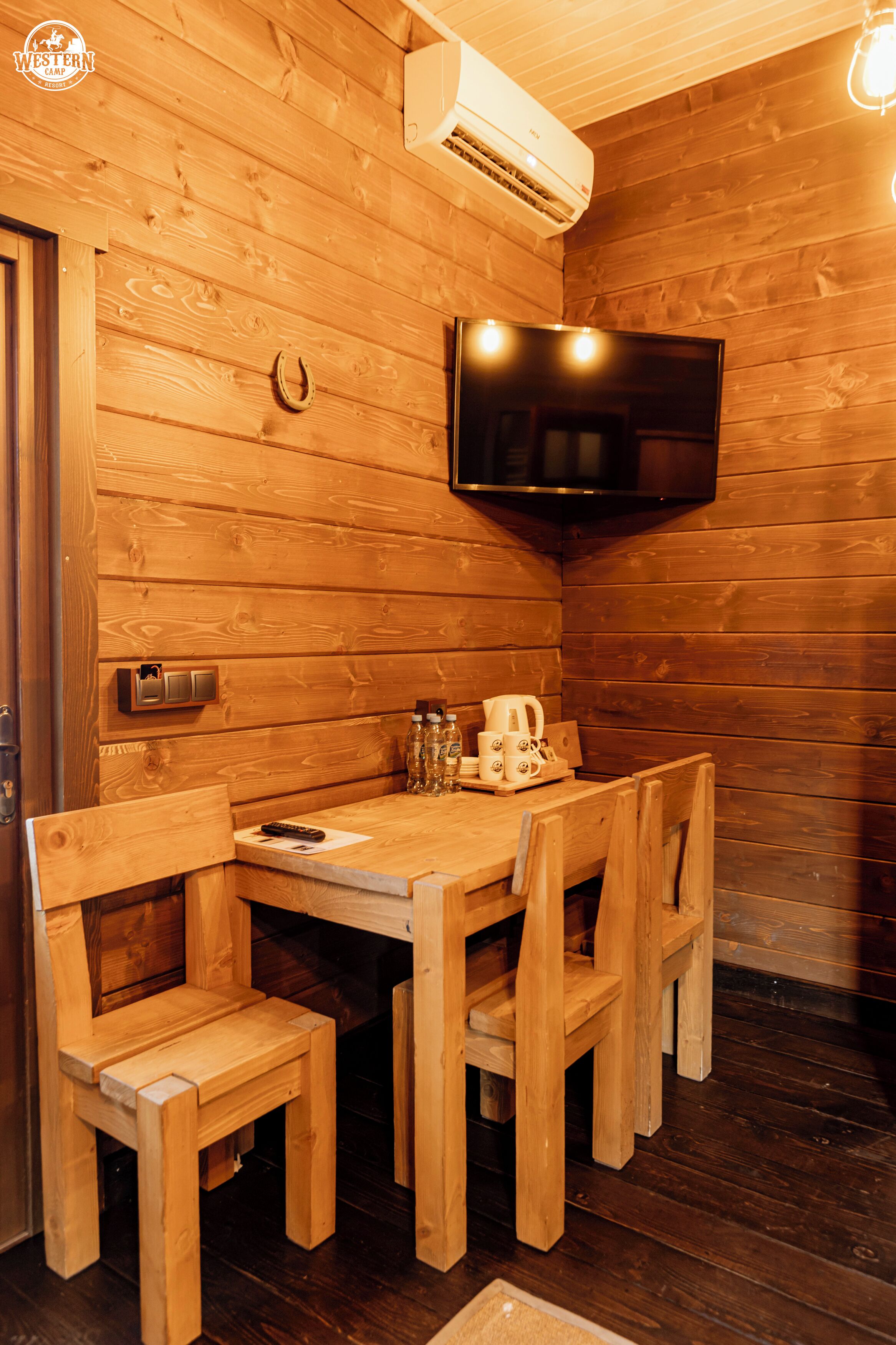 A wooden interior with a dining table, chairs, a mounted television, and an air conditioning unit.
